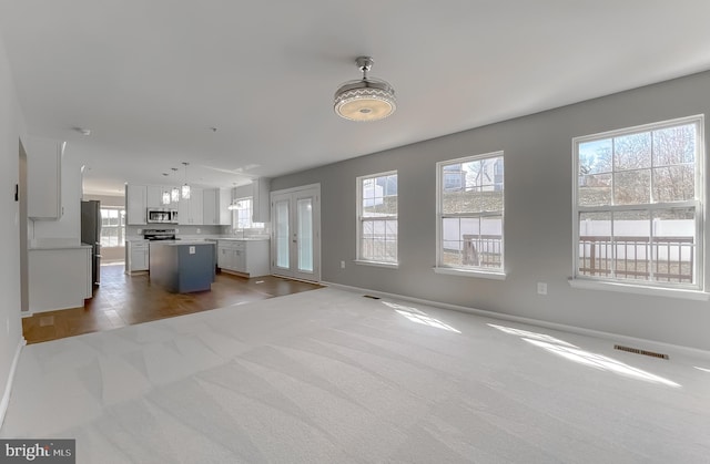 unfurnished living room featuring a wealth of natural light, visible vents, and baseboards