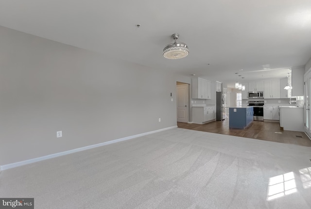 unfurnished living room featuring carpet floors, baseboards, and a sink