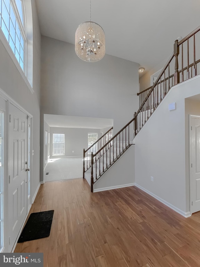 entryway with wood finished floors, a high ceiling, stairs, a notable chandelier, and a wealth of natural light