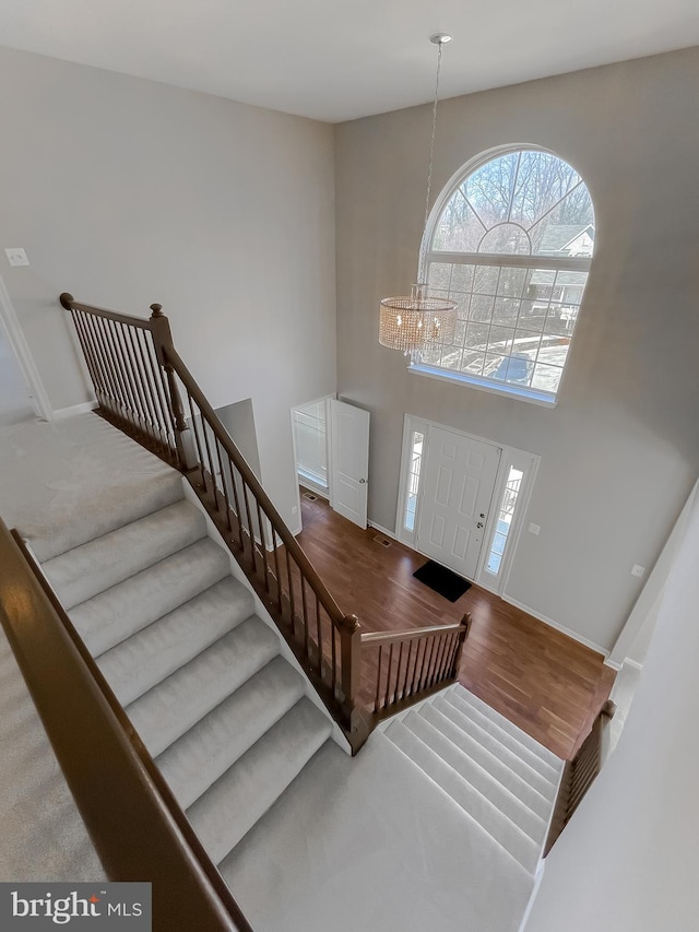 entryway featuring a notable chandelier, wood finished floors, stairway, baseboards, and a towering ceiling