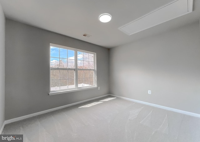 carpeted spare room featuring visible vents, attic access, and baseboards