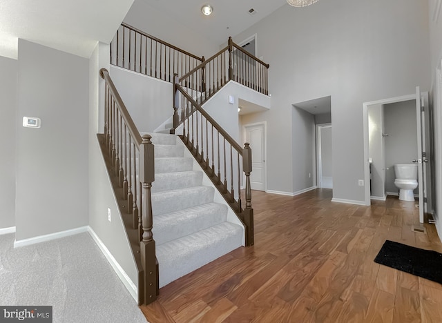 stairway featuring visible vents, baseboards, a high ceiling, and wood finished floors