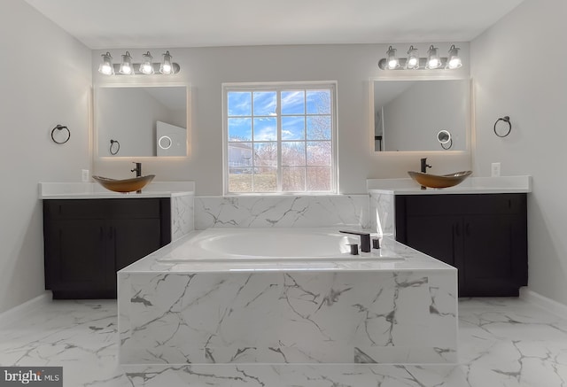 full bath with a sink, a garden tub, marble finish floor, and two vanities