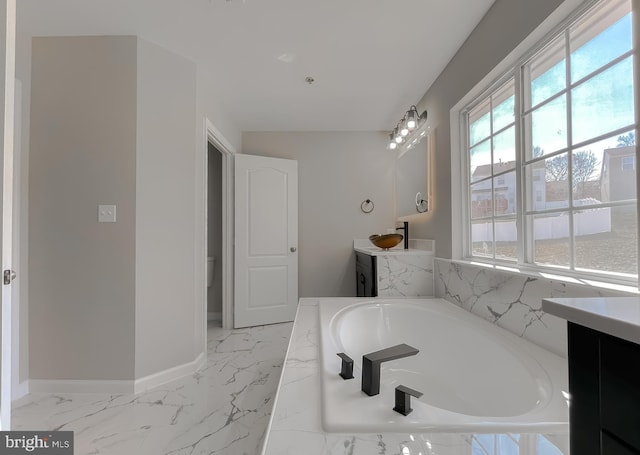 bathroom with baseboards, marble finish floor, vanity, and a garden tub