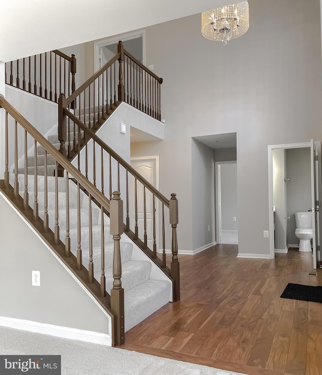 stairway featuring an inviting chandelier, a high ceiling, wood finished floors, and baseboards