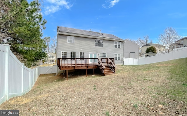 rear view of property featuring a gate, solar panels, a fenced backyard, a deck, and a lawn