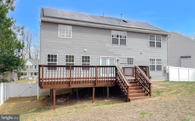 back of property with a fenced backyard, solar panels, and a deck