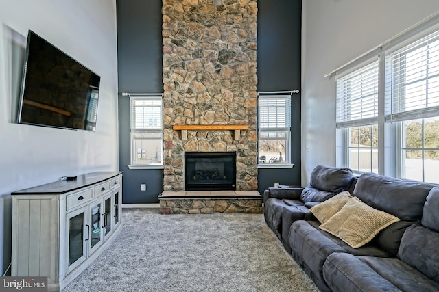 carpeted living room featuring plenty of natural light, a stone fireplace, and a towering ceiling