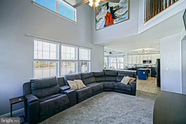 living room with light tile patterned floors, light colored carpet, a towering ceiling, and ceiling fan