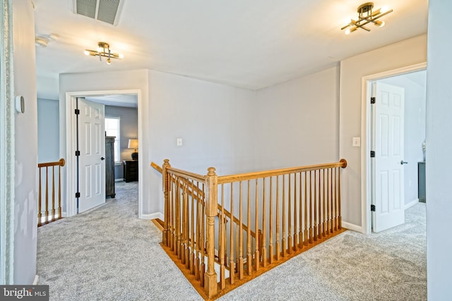 hall featuring an upstairs landing, visible vents, and carpet floors