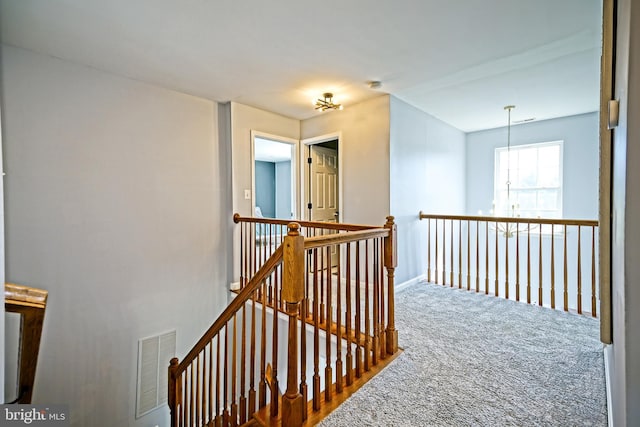 hallway with carpet flooring, an upstairs landing, visible vents, and baseboards