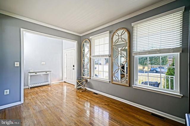 empty room featuring visible vents, wood finished floors, baseboards, and ornamental molding