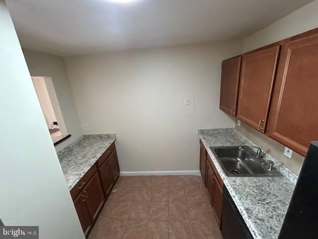 kitchen with light tile patterned flooring, brown cabinetry, baseboards, and a sink