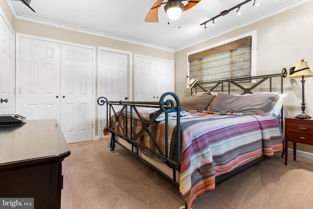 bedroom featuring two closets, light colored carpet, ornamental molding, rail lighting, and a ceiling fan