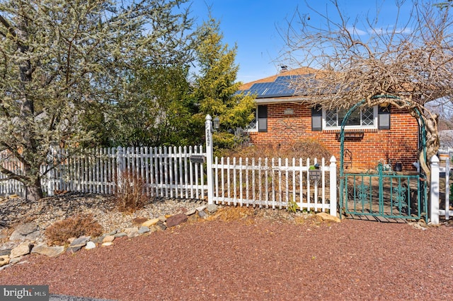 exterior space featuring a fenced front yard, roof mounted solar panels, brick siding, and a chimney