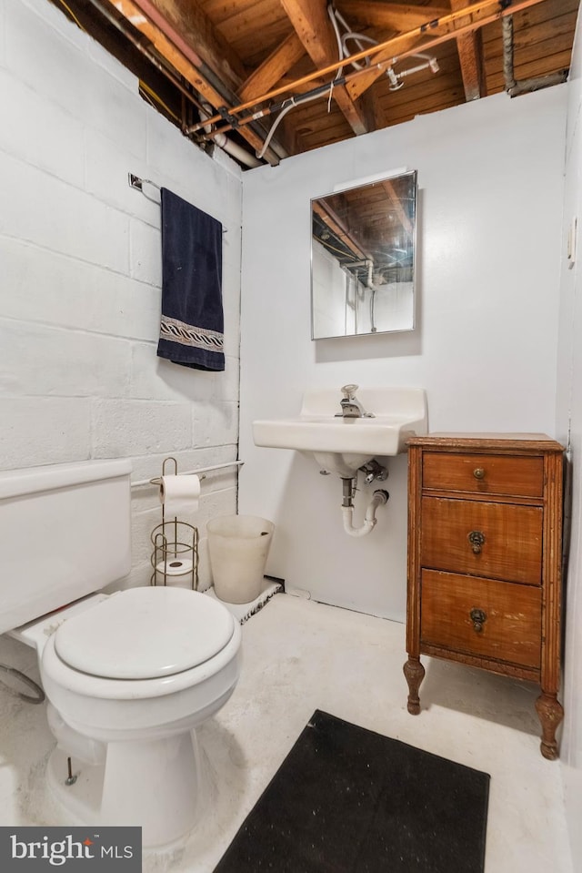 half bath with concrete block wall, toilet, concrete floors, and a sink