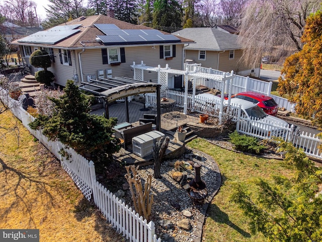 back of house featuring solar panels, a fenced backyard, a lawn, and roof with shingles