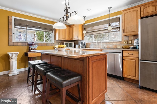 kitchen featuring ornamental molding, appliances with stainless steel finishes, a kitchen bar, backsplash, and a center island