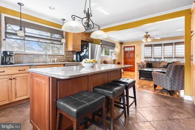 kitchen with freestanding refrigerator, a sink, crown molding, a kitchen breakfast bar, and a center island