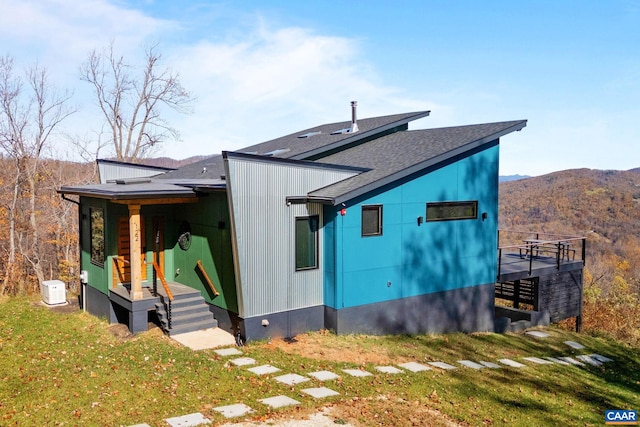 view of side of property with a yard, a mountain view, and roof with shingles