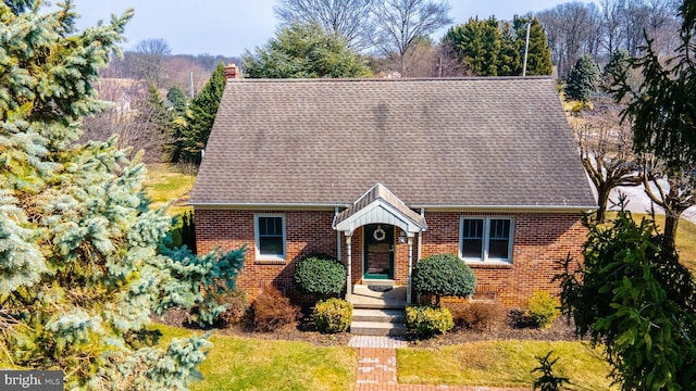 view of front of property featuring brick siding, a chimney, and a shingled roof