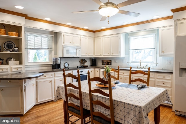 kitchen with light wood finished floors, dark countertops, white appliances, a ceiling fan, and a sink