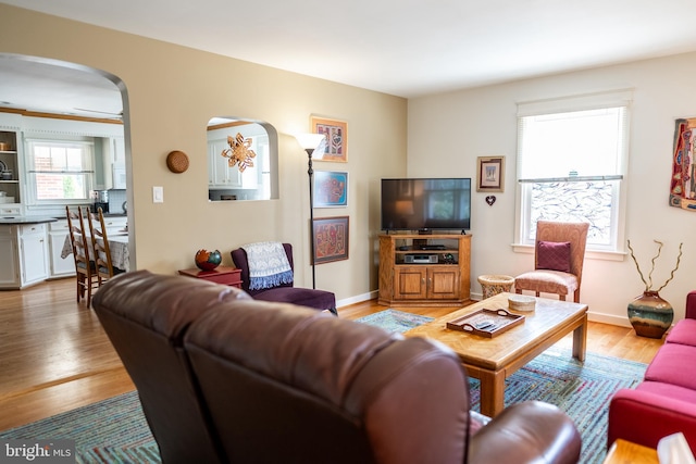 living room featuring light wood-style flooring, baseboards, and arched walkways