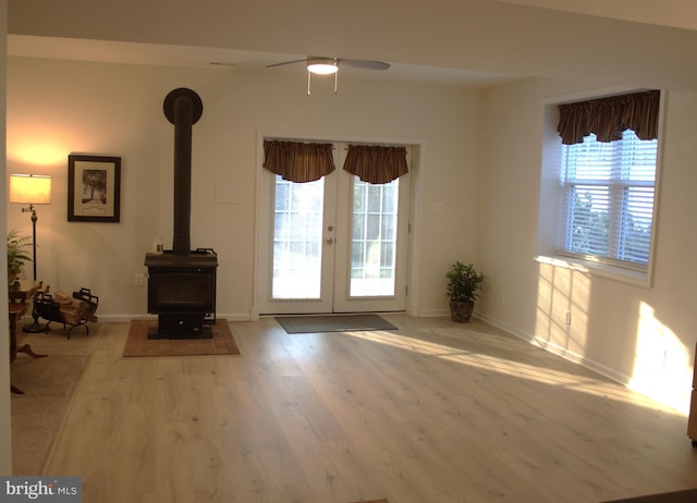 unfurnished living room featuring wood finished floors, french doors, baseboards, ceiling fan, and a wood stove