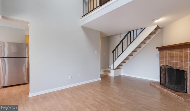 unfurnished living room with stairway, wood finished floors, baseboards, and a fireplace with raised hearth