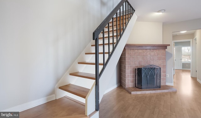 staircase with wood finished floors, baseboards, and a tile fireplace