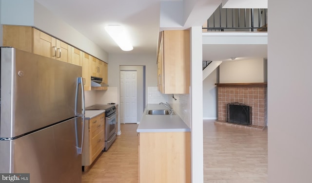 kitchen with light wood finished floors, light brown cabinets, under cabinet range hood, appliances with stainless steel finishes, and a sink