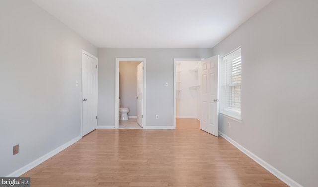 unfurnished bedroom with a spacious closet, baseboards, and light wood-type flooring