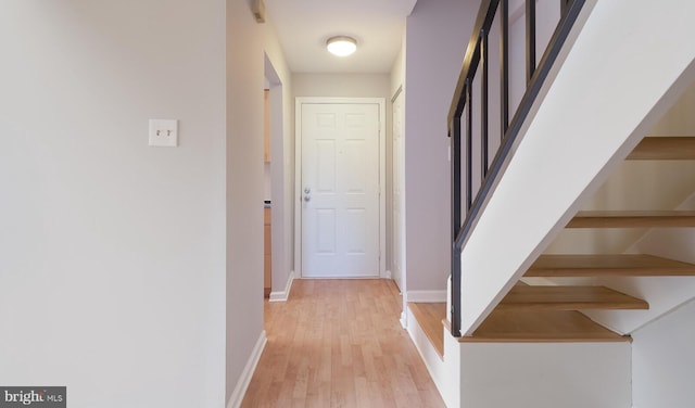 corridor with baseboards, stairs, and light wood finished floors