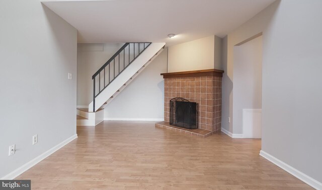 unfurnished living room featuring a tiled fireplace, stairway, light wood-style flooring, and baseboards