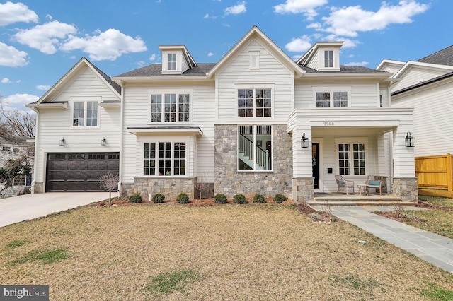 view of front of home with stone siding, fence, an attached garage, driveway, and covered porch