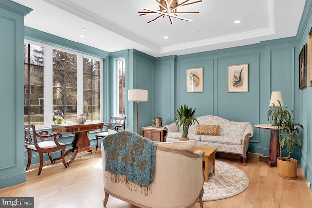 living area with a decorative wall, light wood-style flooring, an inviting chandelier, and crown molding