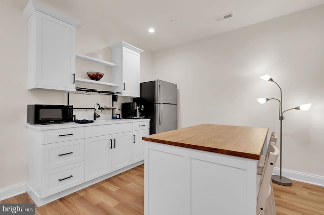 kitchen with open shelves, butcher block countertops, freestanding refrigerator, light wood-style flooring, and black microwave
