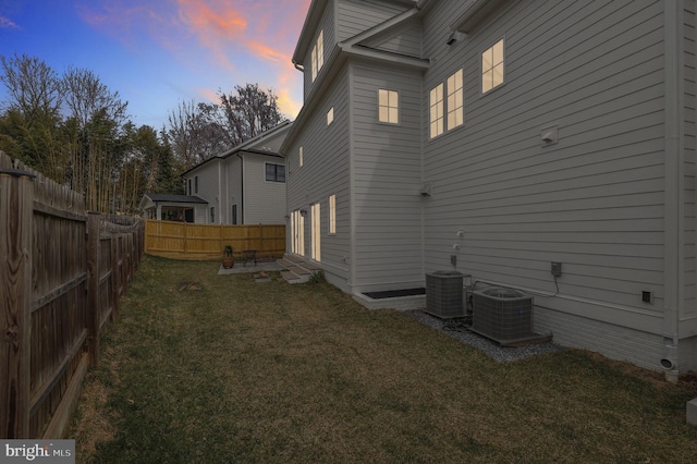 property exterior at dusk featuring a fenced backyard, a lawn, and central AC