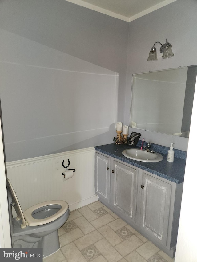 half bath with a wainscoted wall, toilet, and vanity