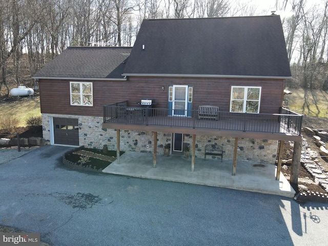 rear view of house with an attached garage, a patio area, stone siding, and driveway