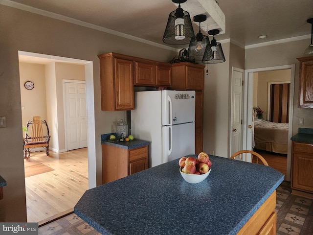 kitchen featuring dark countertops, ornamental molding, freestanding refrigerator, wood finished floors, and brown cabinetry