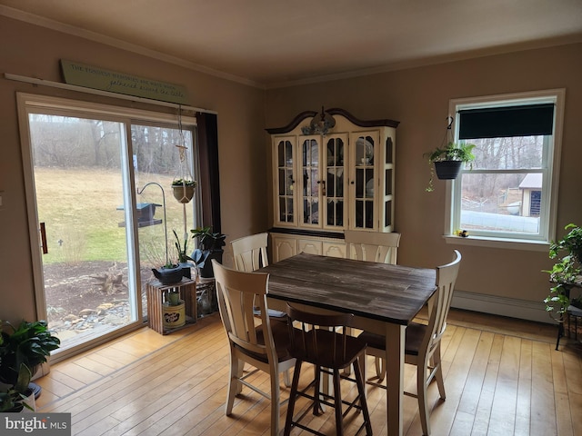 dining room with light wood-style flooring, a healthy amount of sunlight, baseboard heating, and ornamental molding