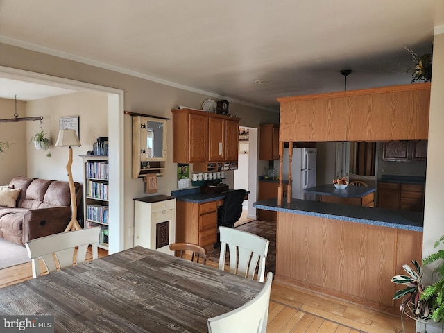 kitchen featuring brown cabinetry, light wood-style flooring, freestanding refrigerator, ornamental molding, and dark countertops