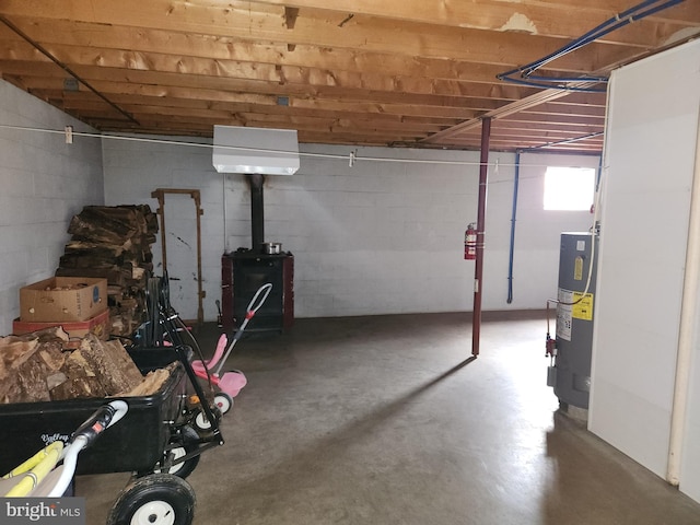 basement featuring a wood stove, concrete block wall, and water heater