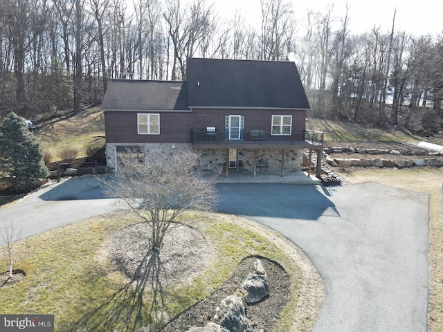 view of front of property with stone siding, driveway, a deck, and a patio