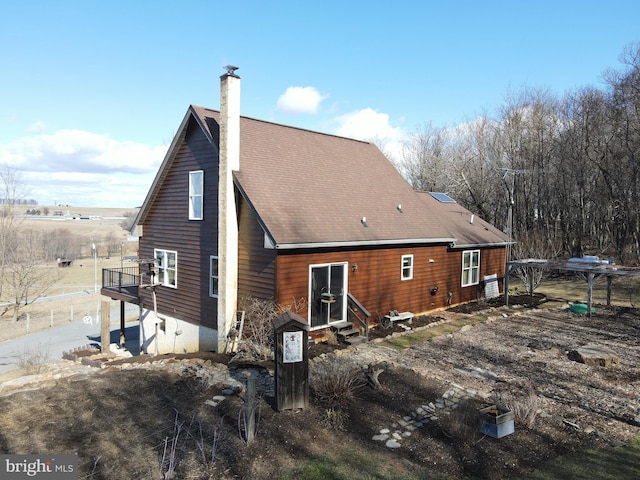 rear view of property with entry steps, a chimney, and roof with shingles