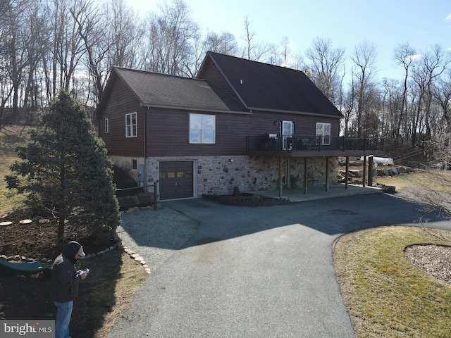 view of front of home with an attached garage, a deck, a patio area, stone siding, and driveway