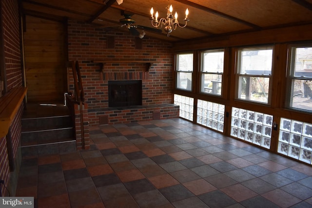 unfurnished living room featuring lofted ceiling with beams, a brick fireplace, ceiling fan with notable chandelier, and brick wall