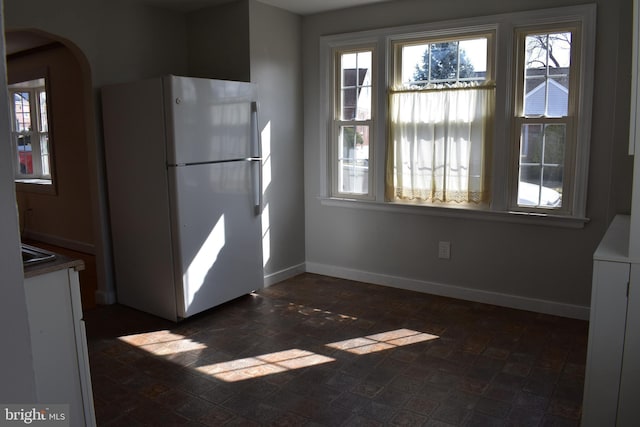 kitchen featuring baseboards, arched walkways, a healthy amount of sunlight, and freestanding refrigerator