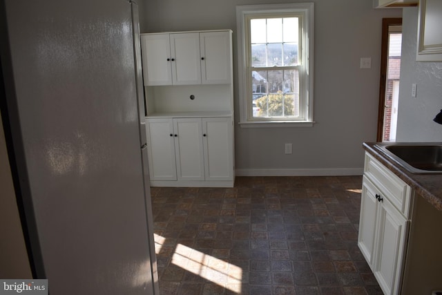 kitchen featuring white cabinets, baseboards, freestanding refrigerator, and a sink